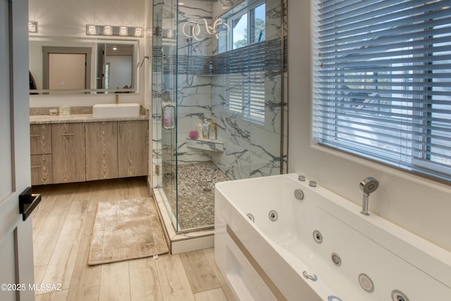 full bath featuring a shower stall, a tub with jets, a sink, and wood finished floors