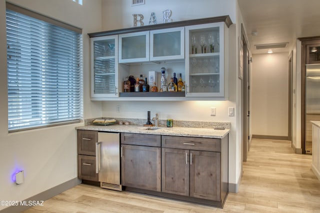 bar with light wood-style flooring, refrigerator, bar area, visible vents, and baseboards