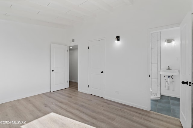 unfurnished bedroom featuring visible vents, ensuite bath, wood finished floors, beamed ceiling, and baseboards