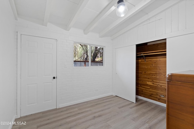 unfurnished bedroom with lofted ceiling with beams, light wood finished floors, brick wall, and a closet