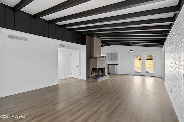 unfurnished living room with visible vents, a fireplace, brick wall, and wood finished floors