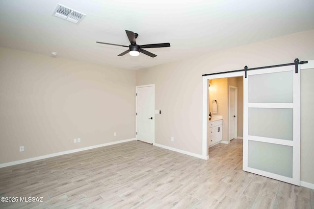unfurnished bedroom with a barn door, visible vents, light wood-style floors, and baseboards
