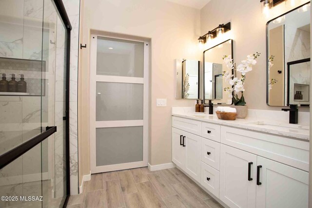 full bathroom with baseboards, a stall shower, double vanity, and a sink
