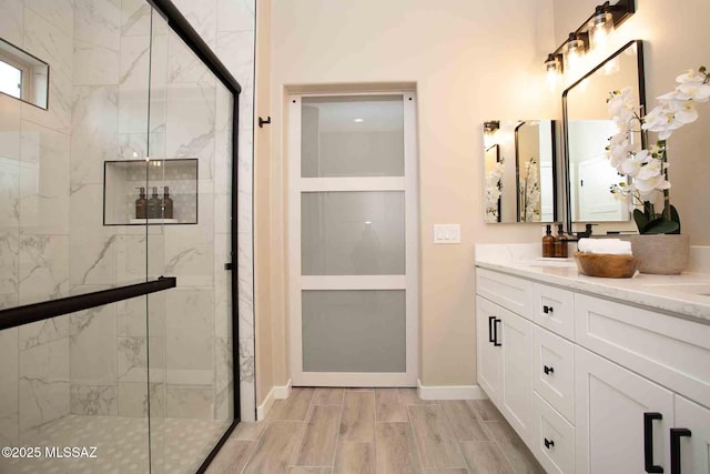 full bath featuring wood tiled floor, double vanity, a shower stall, and baseboards