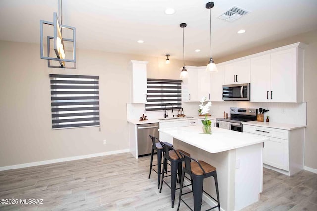 kitchen with stainless steel appliances, white cabinets, a kitchen bar, a sink, and visible vents