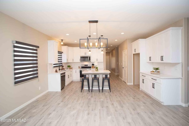 kitchen featuring a sink, a breakfast bar area, light wood-style flooring, white cabinetry, and appliances with stainless steel finishes