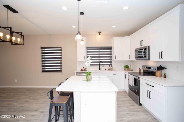 kitchen with stainless steel appliances, backsplash, a sink, white cabinetry, and a center island