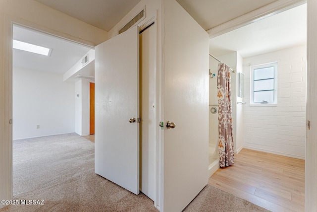 hallway with visible vents, light carpet, and light wood finished floors