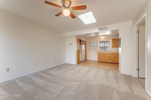 unfurnished living room featuring a skylight, light colored carpet, visible vents, a sink, and ceiling fan