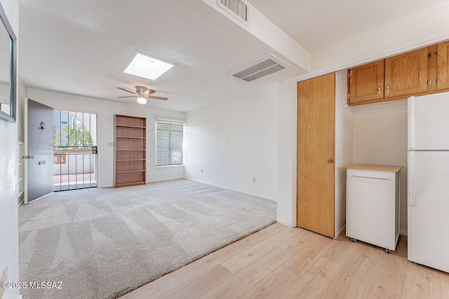 empty room with a skylight, visible vents, light carpet, and light wood finished floors