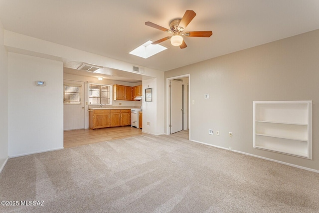 unfurnished living room with built in features, a skylight, light colored carpet, and visible vents