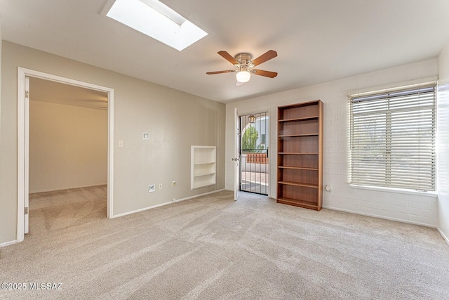 empty room with carpet floors, a skylight, ceiling fan, and built in features