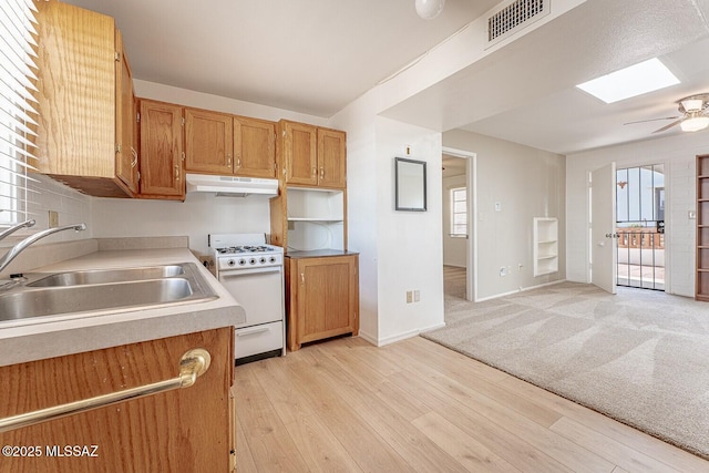 kitchen featuring a skylight, white gas stove, visible vents, a sink, and under cabinet range hood