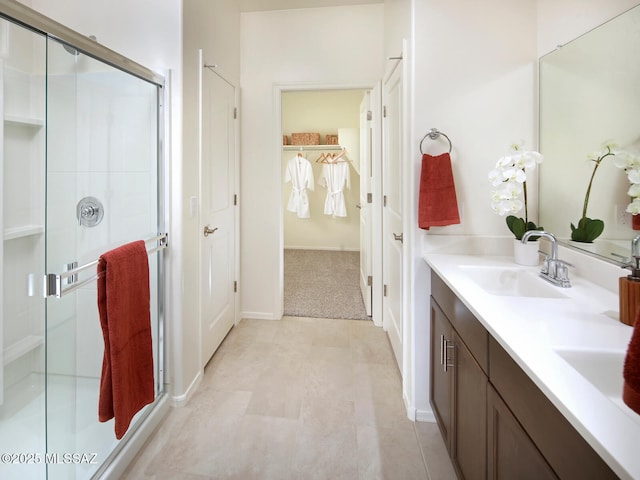 bathroom featuring double vanity, a spacious closet, a stall shower, and a sink