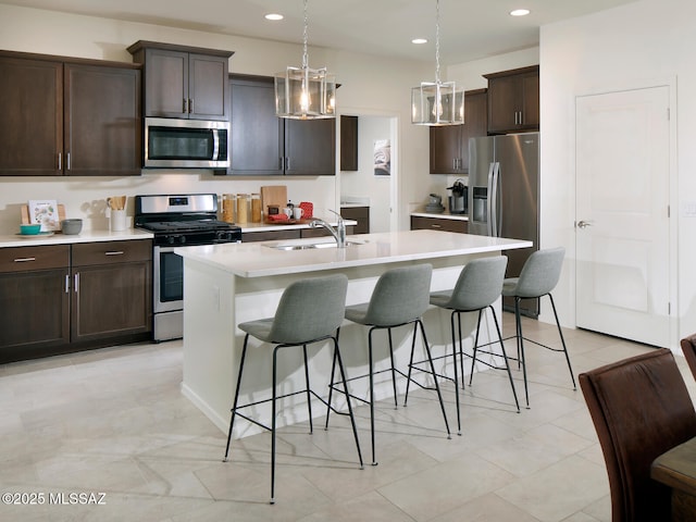 kitchen with a sink, light countertops, appliances with stainless steel finishes, a kitchen bar, and a center island with sink