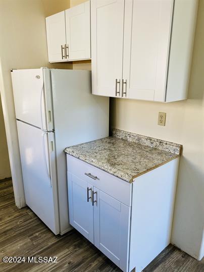 kitchen with light stone counters, dark wood finished floors, freestanding refrigerator, and white cabinets