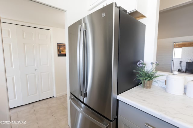 kitchen with light tile patterned flooring, gray cabinetry, freestanding refrigerator, and light stone countertops