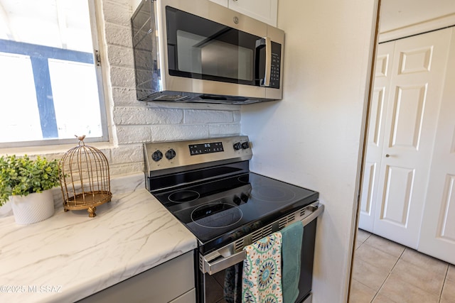 kitchen with light tile patterned floors, light stone countertops, stainless steel appliances, decorative backsplash, and white cabinetry