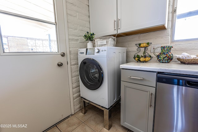 clothes washing area with light tile patterned floors, plenty of natural light, cabinet space, and washer / clothes dryer