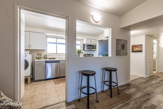 kitchen with light wood-type flooring, decorative backsplash, appliances with stainless steel finishes, a kitchen breakfast bar, and washer / clothes dryer