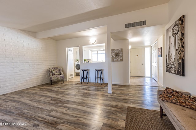 living area with visible vents, beam ceiling, wood finished floors, brick wall, and baseboards