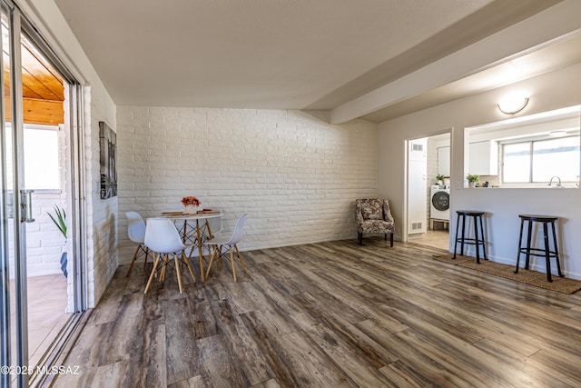 dining space featuring wood finished floors, washer / clothes dryer, and brick wall