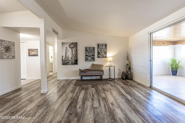 living area featuring baseboards, visible vents, brick wall, dark wood-type flooring, and vaulted ceiling