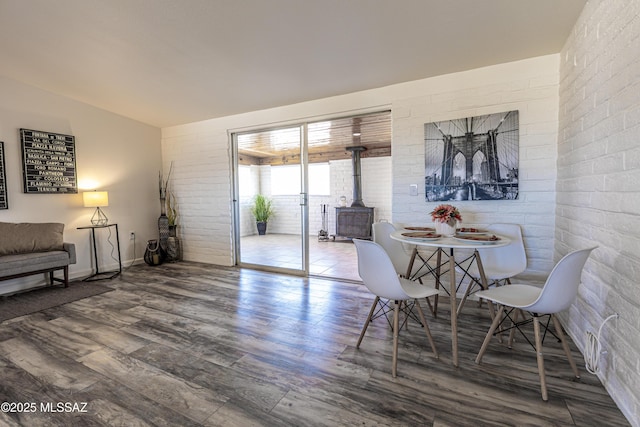 dining space with brick wall, wood finished floors, and a wood stove