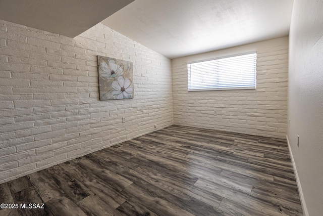 empty room featuring lofted ceiling, brick wall, and dark wood-style flooring