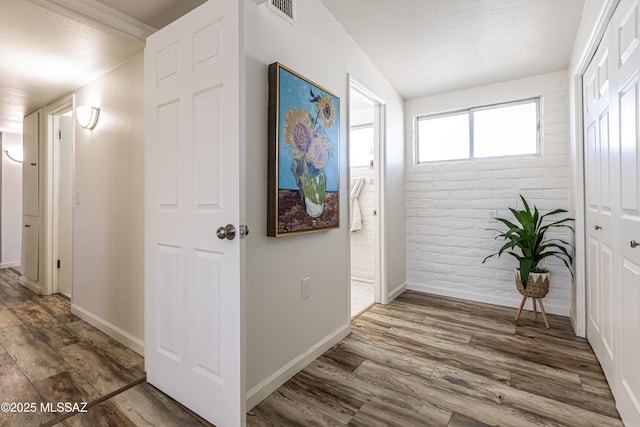 corridor with visible vents, baseboards, wood finished floors, and brick wall