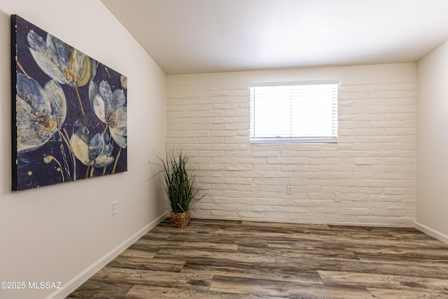 empty room with brick wall, baseboards, and wood finished floors