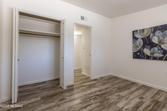 unfurnished bedroom with wood finished floors, visible vents, a closet, and baseboards