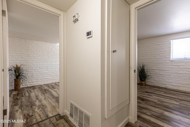 hall featuring visible vents, wood finished floors, and brick wall