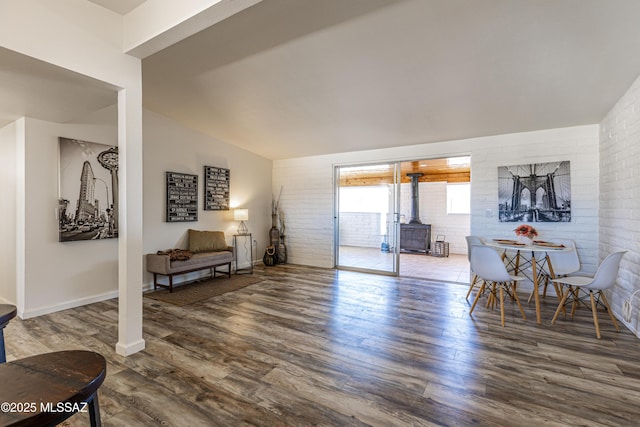 sitting room with vaulted ceiling, brick wall, a wood stove, and wood finished floors