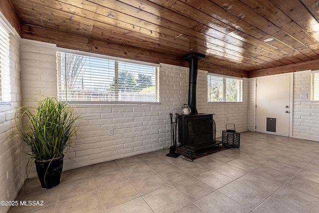 living area featuring a wealth of natural light, brick wall, wood ceiling, and a wood stove