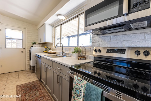 kitchen featuring a sink, separate washer and dryer, appliances with stainless steel finishes, light tile patterned floors, and decorative backsplash