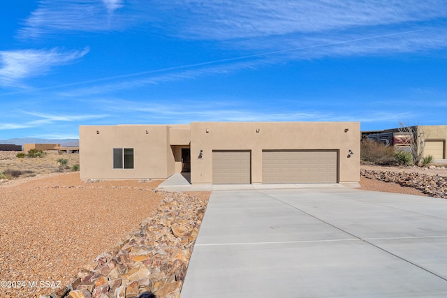 pueblo-style house featuring a garage, concrete driveway, and stucco siding