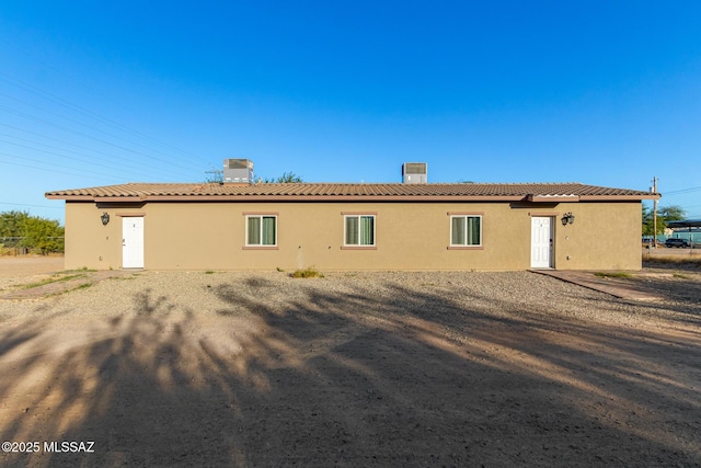 rear view of house with a tile roof, a chimney, and stucco siding