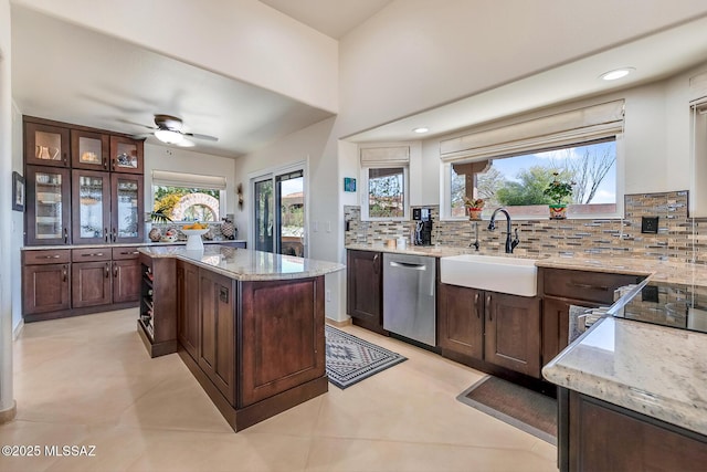 kitchen featuring light stone countertops, dark brown cabinetry, dishwasher, decorative backsplash, and a sink