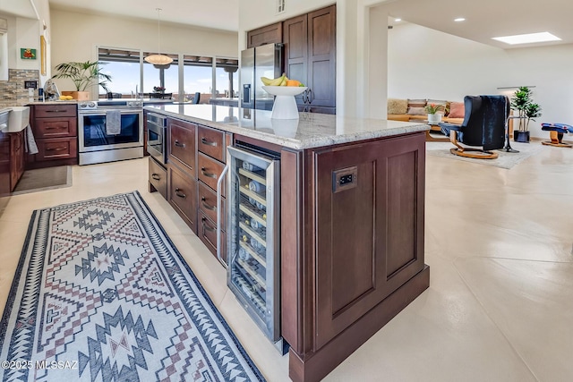 kitchen with light stone countertops, beverage cooler, decorative backsplash, appliances with stainless steel finishes, and a center island