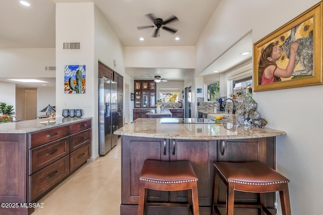 kitchen featuring light stone countertops, visible vents, a peninsula, stainless steel refrigerator with ice dispenser, and black electric stovetop