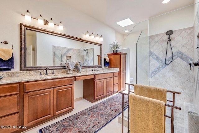 bathroom with double vanity, a skylight, a tile shower, and a sink