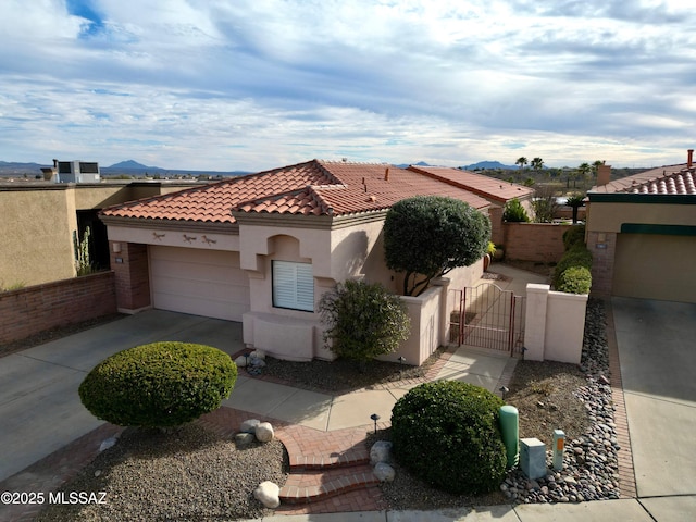 mediterranean / spanish home with a garage, concrete driveway, a tiled roof, a gate, and stucco siding