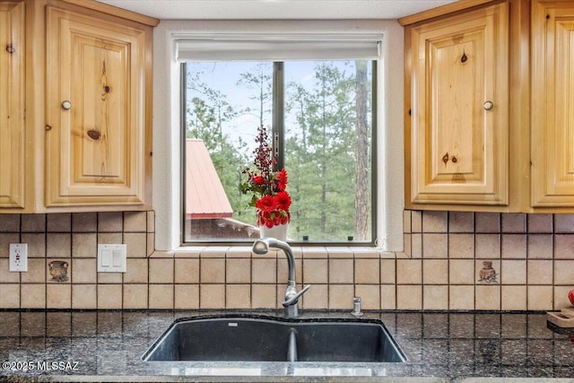 kitchen with dark countertops, light brown cabinets, decorative backsplash, and a sink