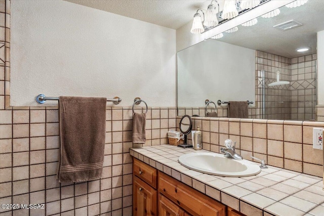 full bathroom with a walk in shower, a textured ceiling, vanity, visible vents, and tile walls