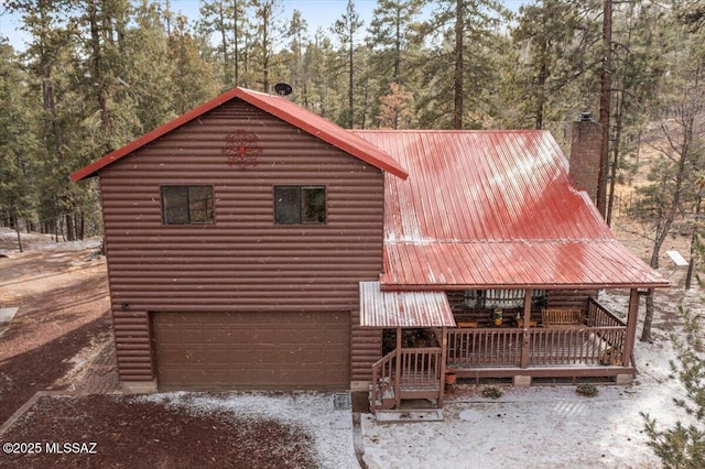 view of front of home with a garage, driveway, faux log siding, a chimney, and metal roof