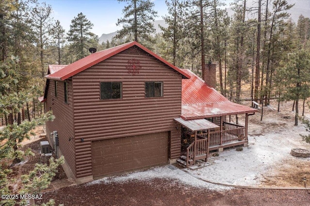 view of side of home featuring covered porch, metal roof, an attached garage, and driveway