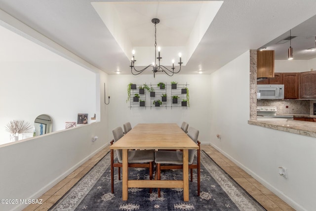 dining area featuring a tray ceiling, light tile patterned flooring, a notable chandelier, and baseboards