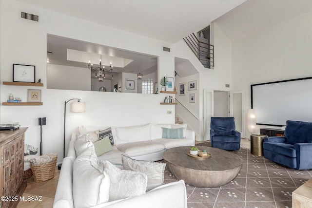 tiled living room with visible vents, stairway, a towering ceiling, and an inviting chandelier