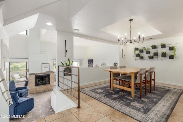 dining room featuring a fireplace, a notable chandelier, a raised ceiling, tile patterned flooring, and baseboards